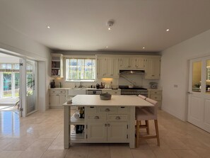 A spacious kitchen with white cabinetry, a central island, and a large window providing natural light. - Luxury 4BDR Retreat With Garden and Workspace (Malahide)