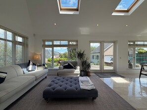 A spacious living room with a large sectional sofa, a dark ottoman, and a potted plant. - Luxury 4BDR Retreat With Garden and Workspace (Malahide)
