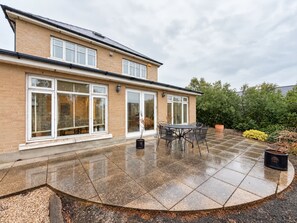 A two-story house with a patio area featuring a table and chairs. - Luxury 4BDR Retreat With Garden and Workspace (Malahide)