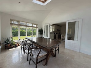 A spacious dining area with a long table and chairs, large windows, and a view of the garden.