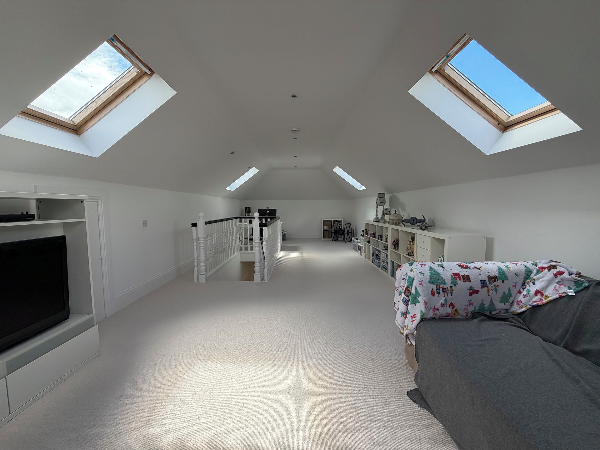 A spacious attic room with skylights, a television, a sofa, and a bookshelf.