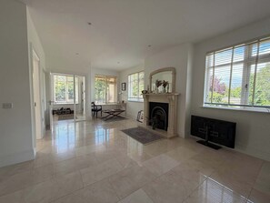 A spacious living room with a fireplace, large windows, and a tiled floor.