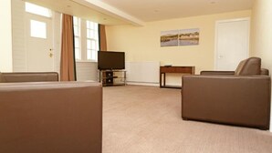 Ein Wohnzimmer mit Fernseher, zwei Sofas, einem kleinen Tisch und einer Tür.