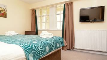 A hotel room with a bed, a television, a window with curtains, and a radiator.