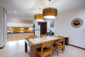 A modern kitchen with wooden cabinets, a dining table with chairs, and pendant lighting. - KUMO 2BR Ocean View Pool - Rooftop (Tambon Hua Hin)