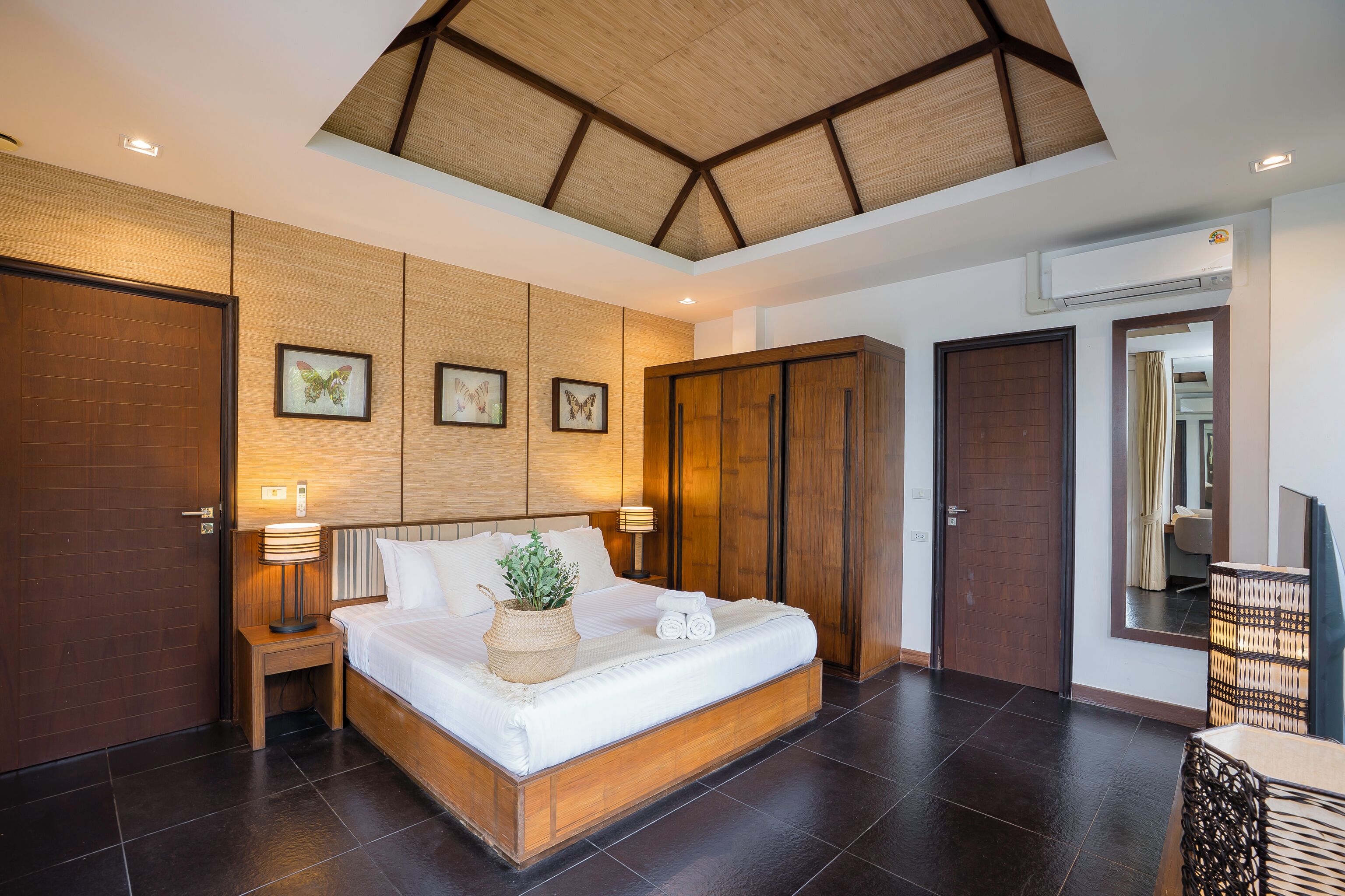 A spacious bedroom with a large bed, wooden headboard, and a ceiling with a wooden beam design.