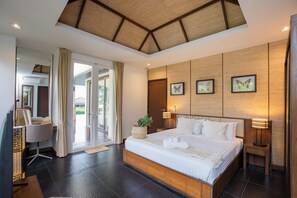 A modern hotel room with a large bed, a desk, a chair, a plant, and a view through the glass door. - KUMO 2BR Ocean View Pool - Rooftop (Tambon Hua Hin)