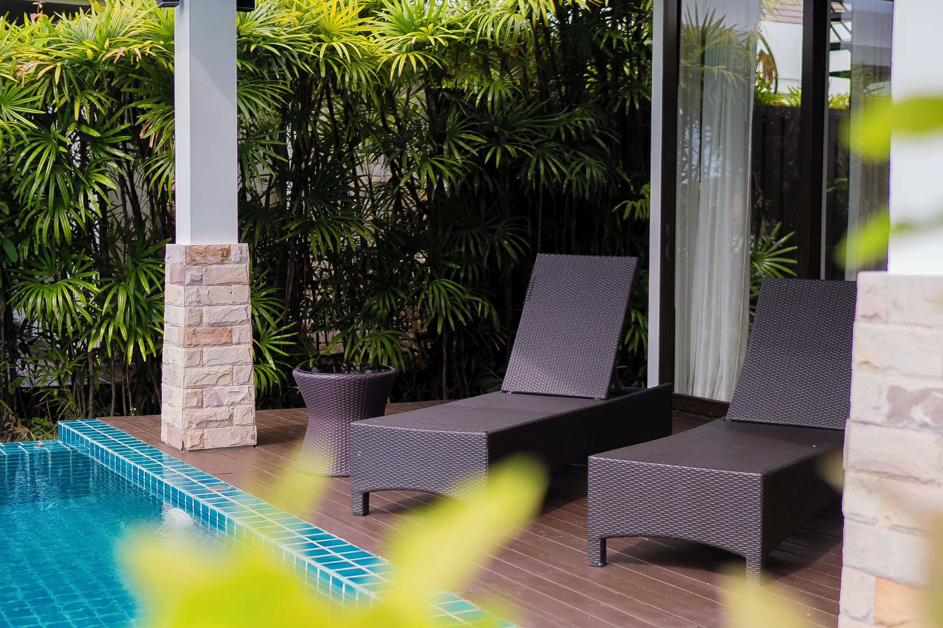 A poolside area with lounge chairs, a stone pillar, and lush greenery.