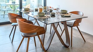 Uma sala de jantar moderna com mesa de vidro, cadeiras de madeira e um lustre peculiar.
