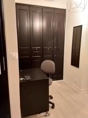 Ein Zimmer mit Schreibtisch, Stuhl, Kleiderschrank und Spiegel.