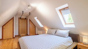 Un dormitori amb sostre inclinat, un lucernari, un llit amb roba de llit estampada, sòls de fusta i una nitriu amb una làmpada.