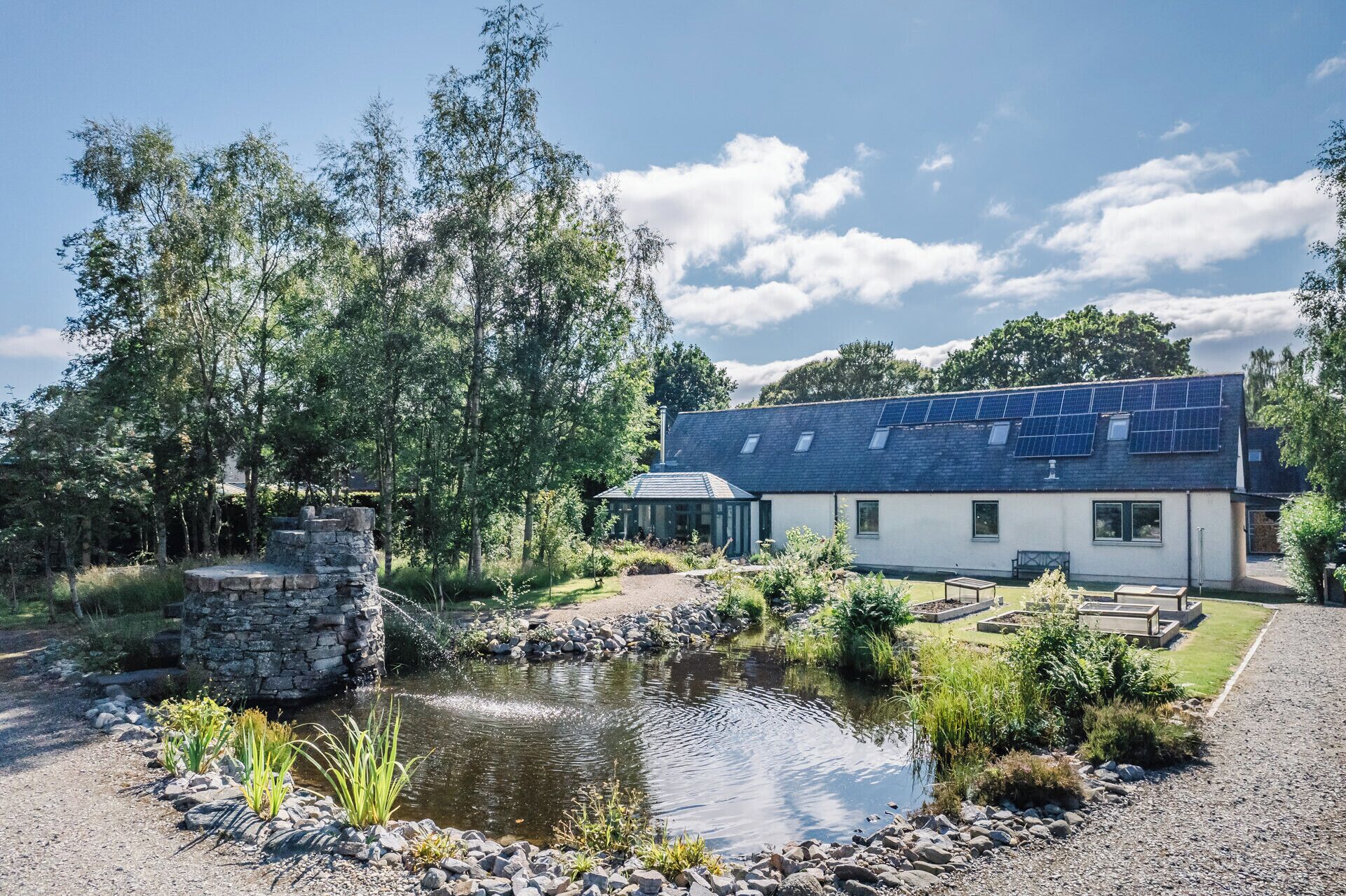 Una casa moderna con techo de paneles solares, estructura de piedra y un estanque.