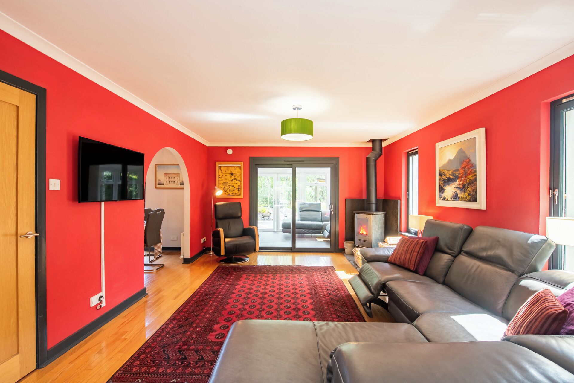 Een woonkamer met een rode muur, een open haard, een bank, een televisie en een groot raam.