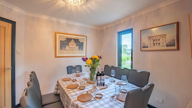 A dining room with a checkered tablecloth, chairs, a vase with flowers, and framed pictures on the walls.