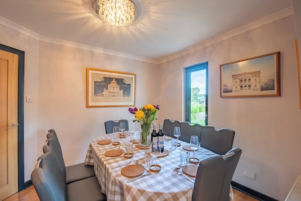 A dining room with a checkered tablecloth, chairs, a vase with flowers, and framed pictures on the walls.