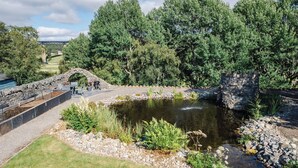 A stone bridge, a pond, and a stone wall with a seating area.