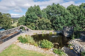A stone bridge, a pond, and a stone wall with a seating area.
