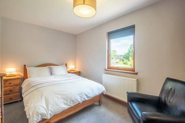 A bedroom with a bed, bedside lamps, a window with a view, a radiator, and a leather chair.