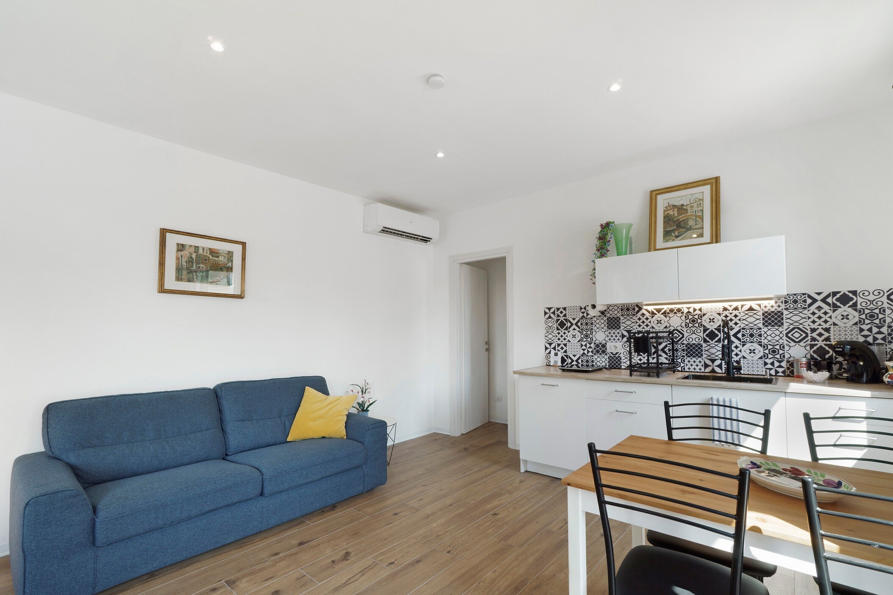 Un salon moderne avec un canapé bleu, une table à manger avec des chaises, une cuisine avec un dosseret décoré et un plafond blanc.
