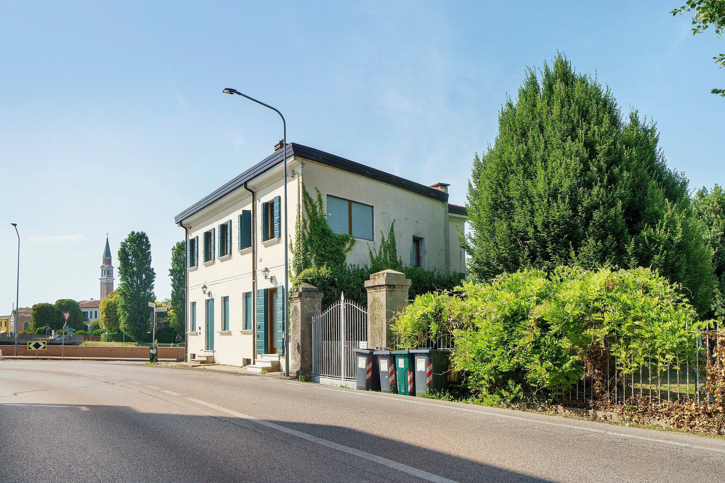 Een gebouw met twee verdiepingen, een witte gevel, een hek en een straat ervoor.
