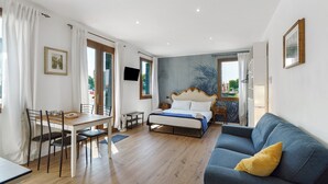 Ein Schlafzimmer mit Bett, Sofa, Esstisch mit Stühlen, Fernseher und einem Fenster mit Vorhängen.