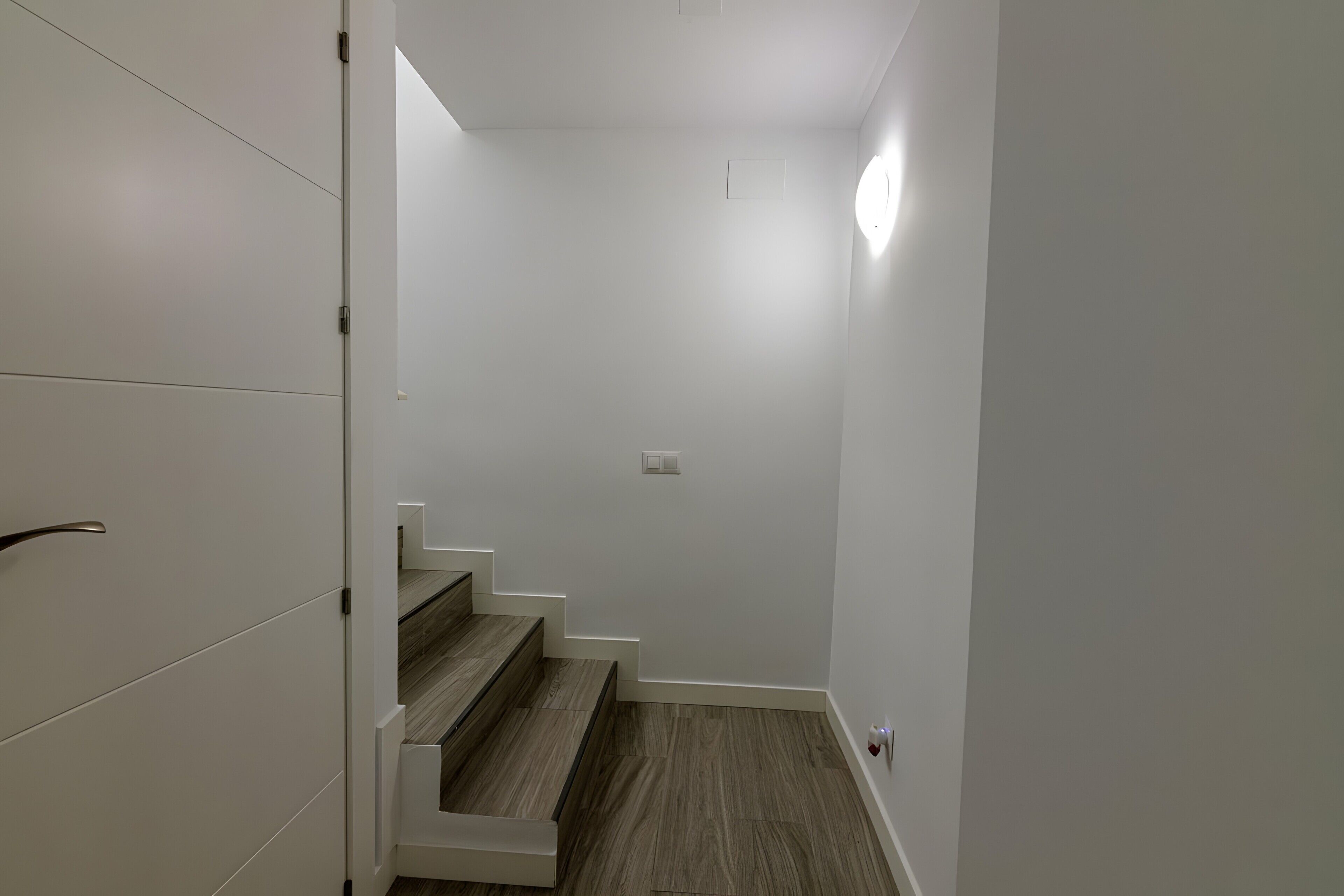 Una escalera de madera con paredes blancas que conduce a un rellano con una lámpara.