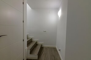 Una scala con gradini in legno e pareti bianche, che conduce a un pianerottolo con un lampadario.