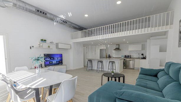 A modern living space with a dining area, a sofa, kitchen, and a TV.