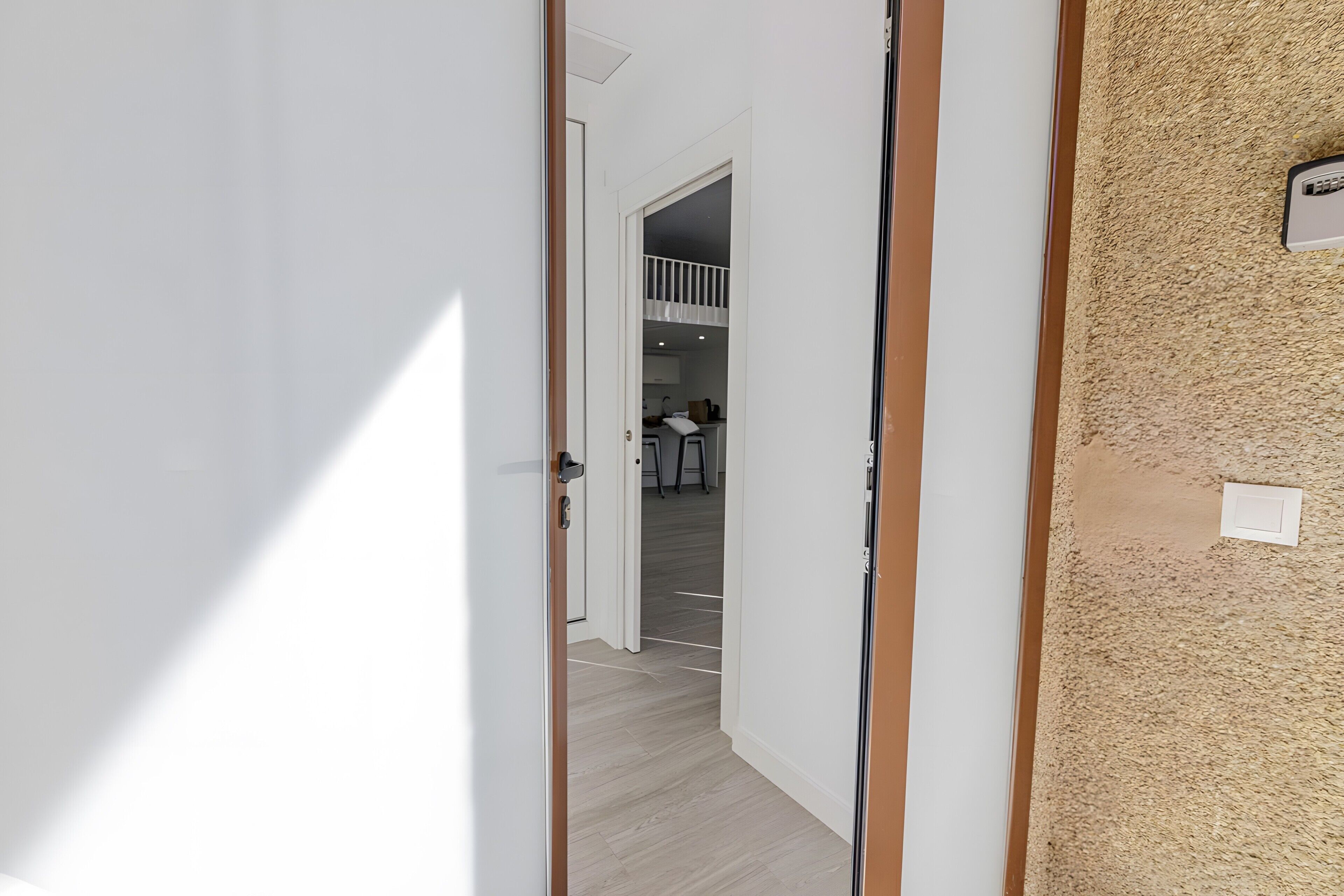 Un pasillo con piso de madera, paredes blancas y una puerta que da a una habitación con kitchenette.