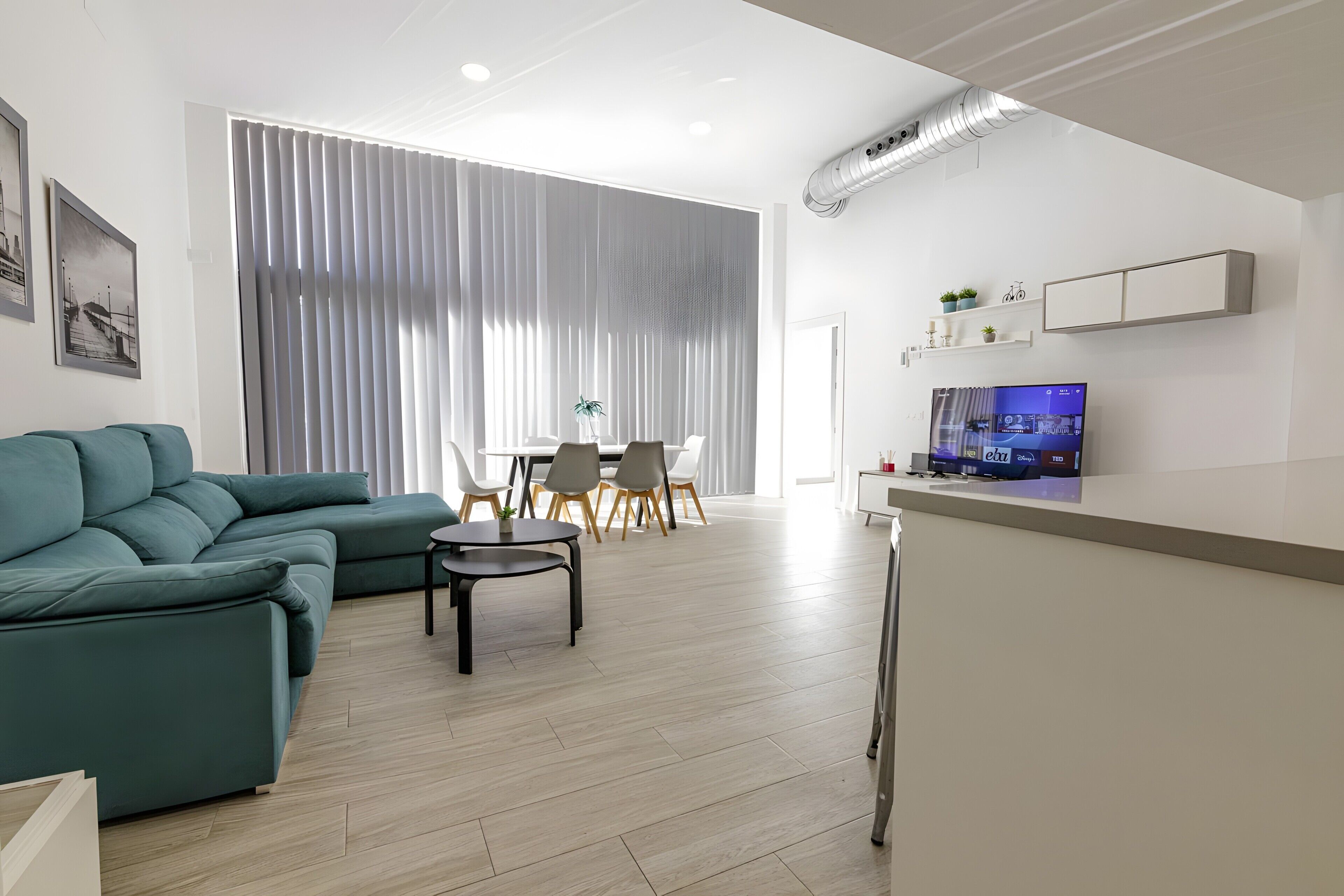Una sala de estar moderna con un sofá modular, un comedor con sillas y un televisor montado en la pared.