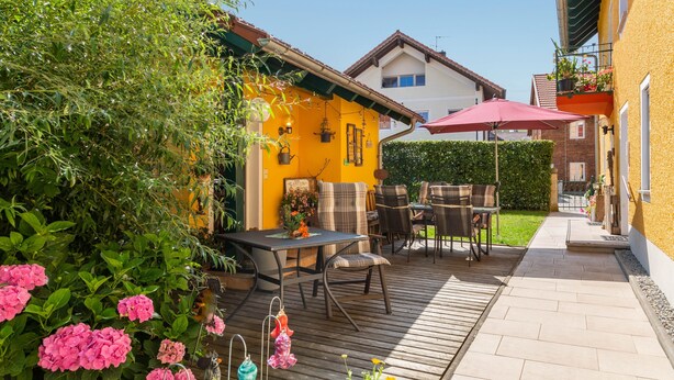 A patio with a wooden table and chairs, surrounded by greenery and flowers. - Doppelhammer Apartment House (Bad Füssing)