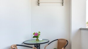 A corner with a small round table, two wicker chairs, a vase with flowers, and a metal shelf. - Doppelhammer Apartment House (Bad Füssing)