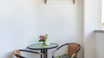 A corner with a small round table, two wicker chairs, a vase with flowers, and a metal shelf.