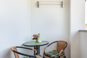 A corner with a small round table, two wicker chairs, a vase with flowers, and a metal shelf. - Doppelhammer Apartment House (Bad Füssing)