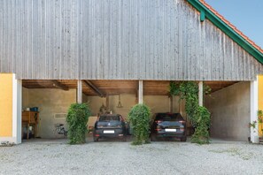 A covered garage with two cars parked inside, a bicycle, and a wooden cabinet.