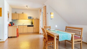 A compact kitchen with wooden cabinets, a microwave, and a dining area with a table and chairs. - Doppelhammer Apartment House (Bad Füssing)
