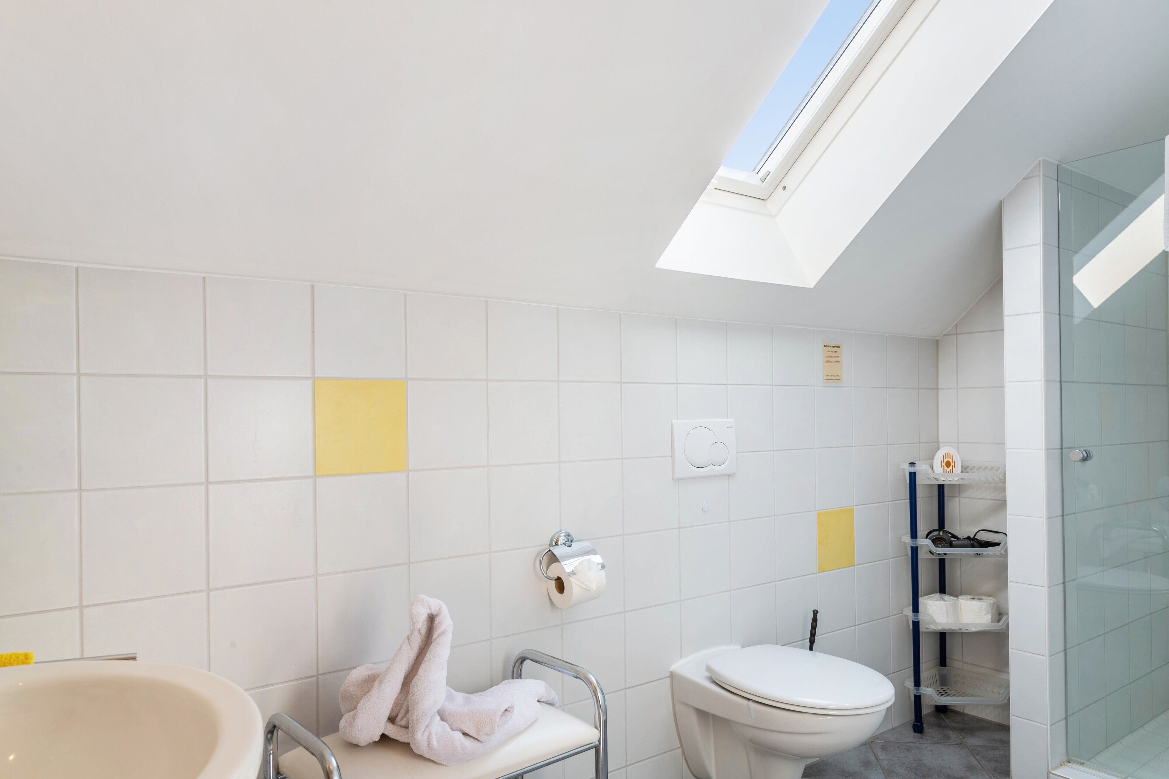 A modern bathroom with a skylight, a bathtub, a toilet, and a glass shower enclosure.