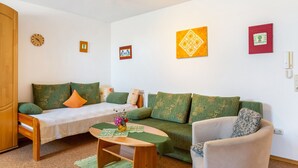 A small, cozy room with a bed, a sofa, and a chair. There are wall-mounted clocks and framed pictures. - Doppelhammer Apartment House (Bad Füssing)