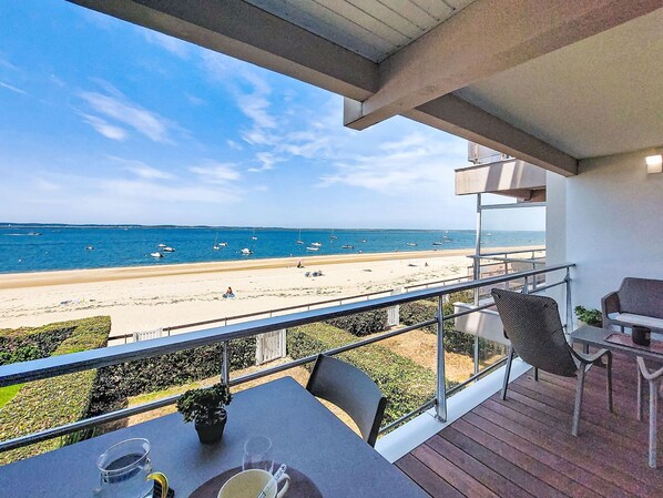 Un balcón con vista a la playa y al océano, una mesa con sillas y una planta en maceta.