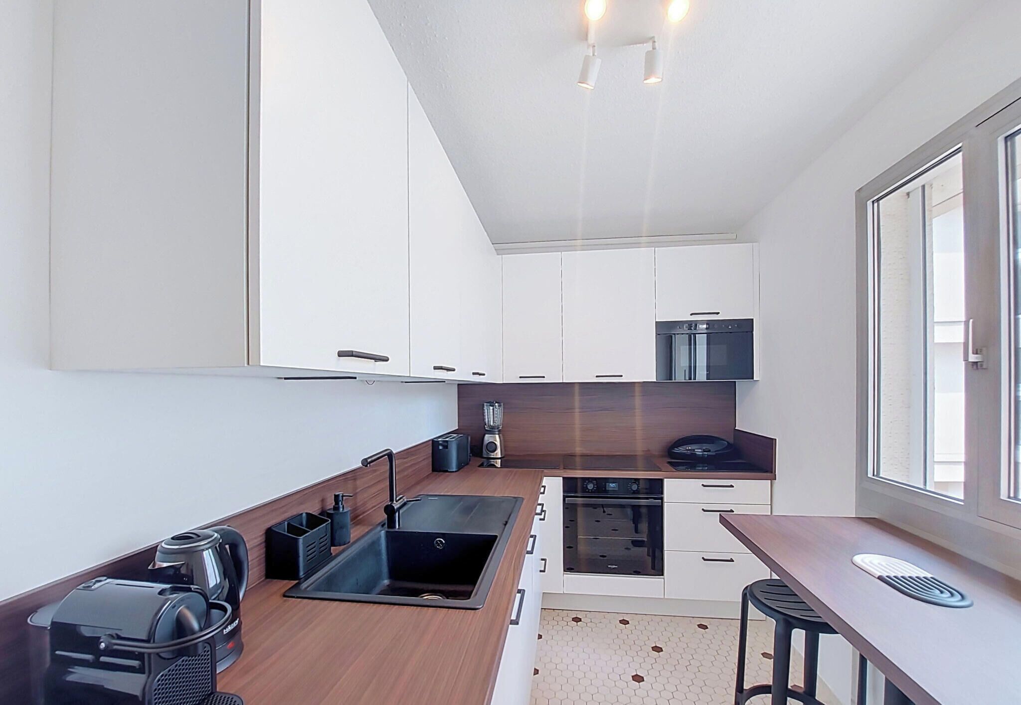 A modern kitchen with a sink, stove, and microwave. There is a window providing natural light.
