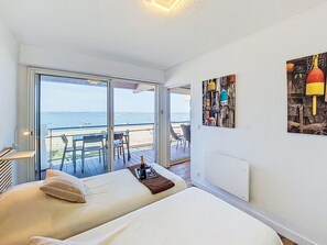 Un dormitorio con cama, mesita de noche, silla y vista al mar a través de una puerta corrediza.