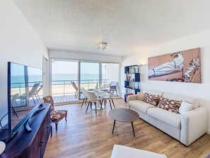 A living room with a TV, sofa, coffee table, and a balcony with a view of the sea. - Apartment Joigny by Interhome (Arcachon)