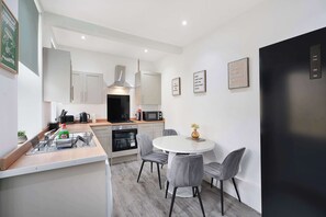 A modern kitchen with a dining area, featuring a central island, grey chairs, and a black refrigerator. - Spacious 4BR Darlington Sleeps 8 by Stay with us (Darlington)