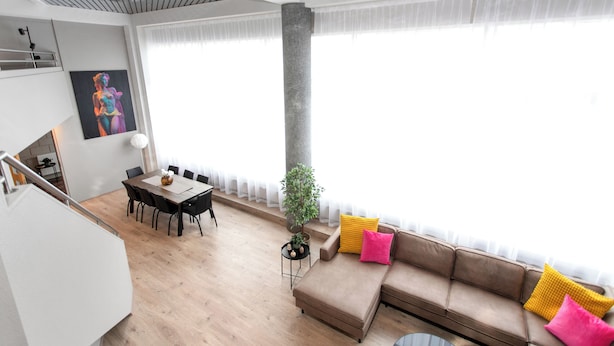 A modern living room with a dining area, a large window, and a staircase.