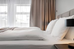 A neatly made bed with white linens, a bedside lamp, and a view of the outdoors through sheer curtains. - Loft 21 - Stylish Five Bedroom Apartment (Reykjavík)