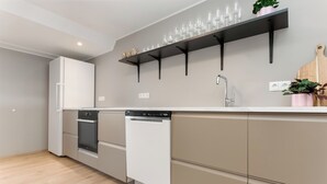 A modern kitchen with a dishwasher, oven, and a shelf holding glasses and a plant.