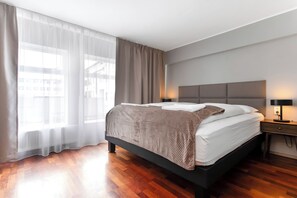 Ein modernes Hotelzimmer mit einem großen Bett, einem Nachttisch, einer Lampe und transparenten Vorhängen.