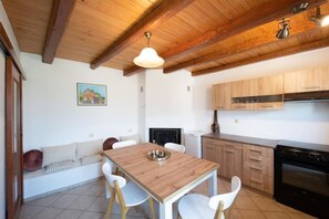 A kitchen with wooden cabinets, a dining table with chairs, a hanging light fixture, and a stove. - Costas Vlachos Appartement (Corfu)