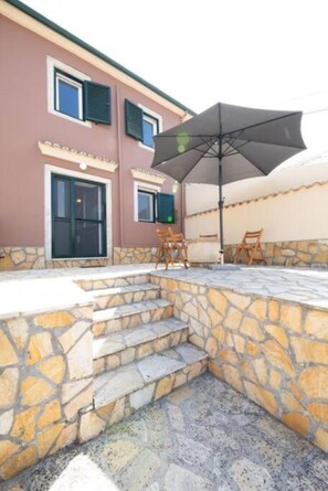A building with a stone staircase leading to a covered patio area with outdoor furniture. - Costas Vlachos Appartement (Corfu)