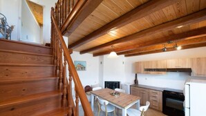 Una escalera de madera conduce a un comedor con una mesa y sillas, una cocina con armarios de madera y un refrigerador blanco.